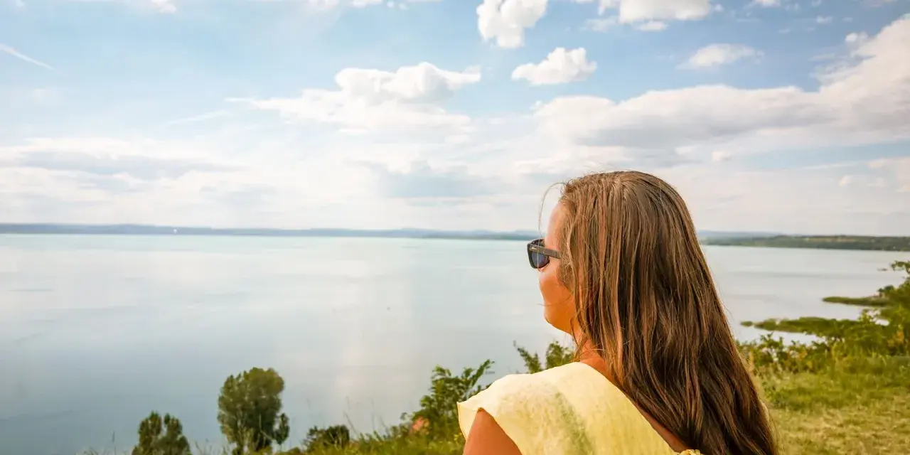 Kobieta w żółtej bluzce podziwia rozległe jezioro Balaton.