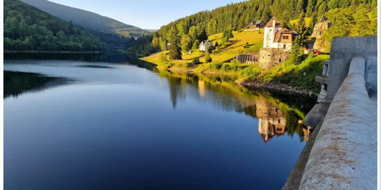 Spokojna tafla jeziora odbija zamek i zalesione wzgórza czeskich Karkonoszy.