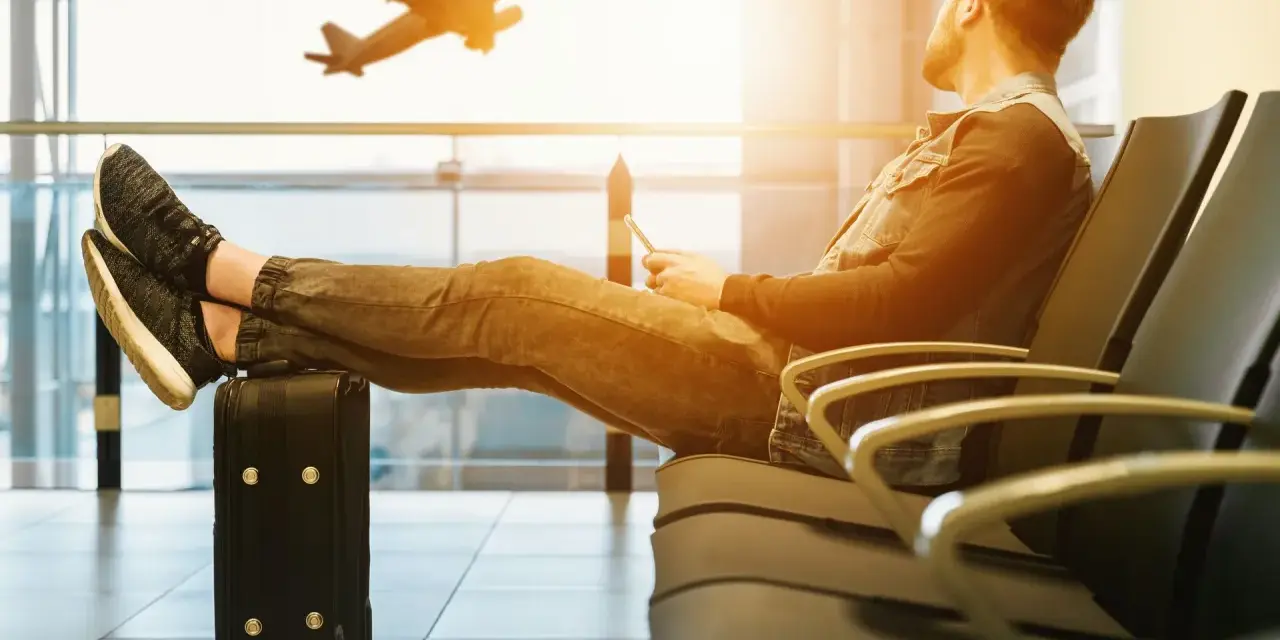 Mężczyzna z nogami na walizce czeka na lotnisku. Samolot startuje. Czyżby czekał na niego, czy to tylko efekt **overbooking**?