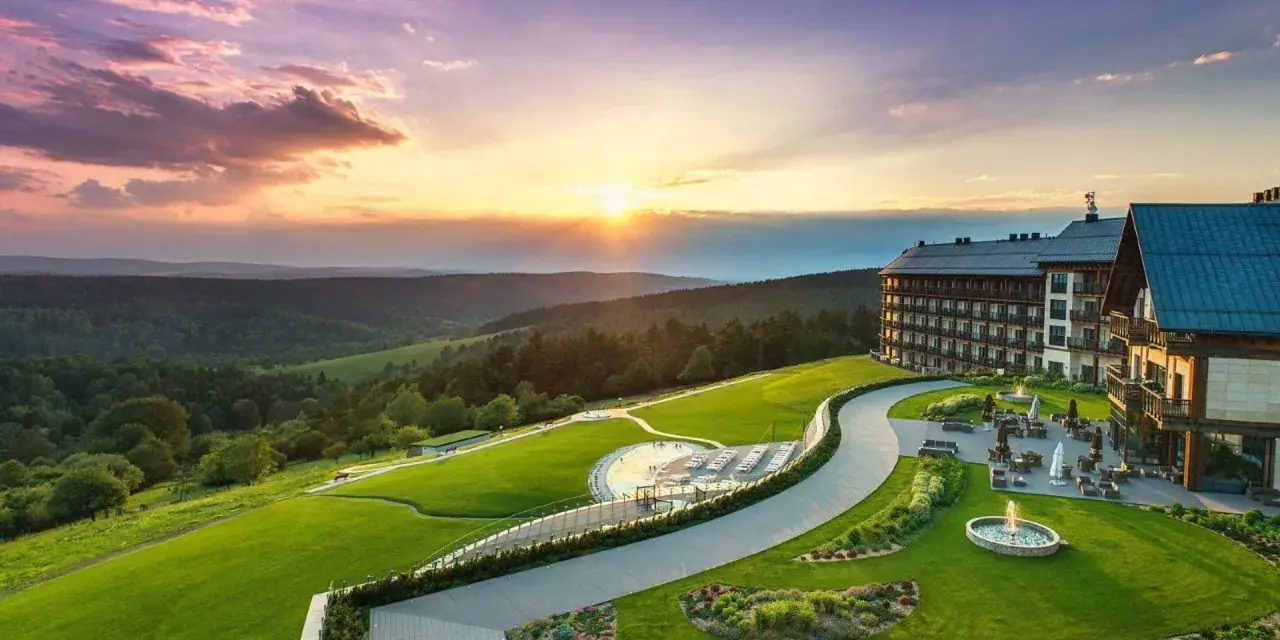 Hotel Arłamów z basenem i tarasem, otoczony zielonymi wzgórzami o zachodzie słońca. Ile pokoi ma hotel Arłamów? Tego nie widać, ale jest ich wiele!
