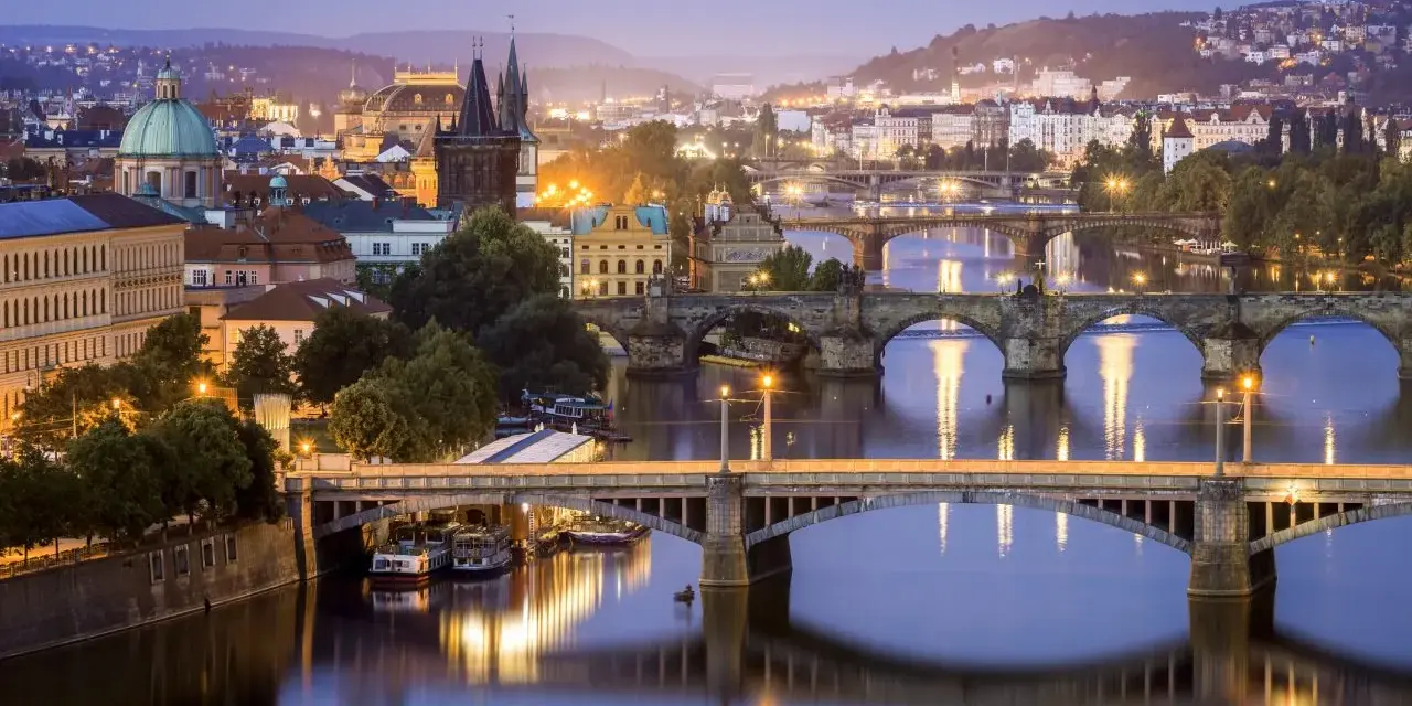 Praga nocą, z wieloma mostami na Wełtawie i oświetlonymi budynkami. Ciekawe ciekawostki o Czechach czekają na odkrycie w tym magicznym mieście.