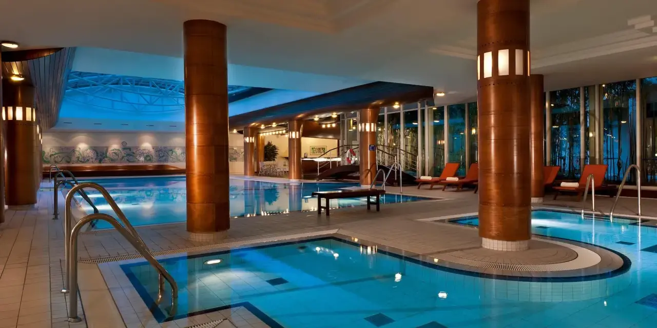 Basen hotelowy Radisson Blu Radebeul z niebieską wodą, drewnianymi kolumnami i leżakami.