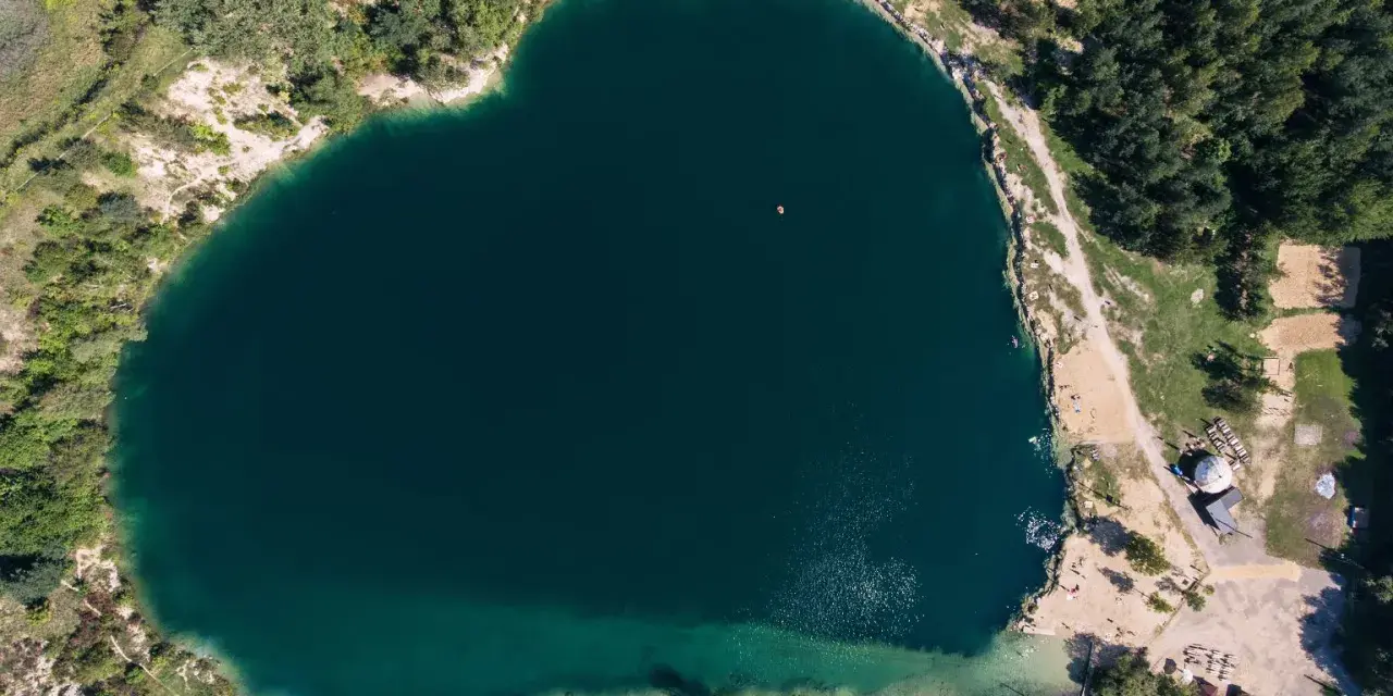 Serce polskiego balatonu, turkusowa woda, otoczona zielenią i piaszczystymi plażami. W oddali widać małą łódkę.
