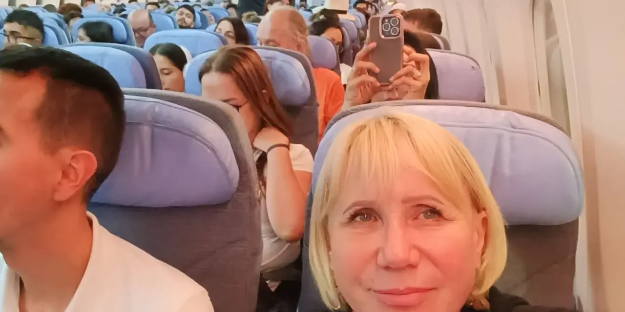 W samolocie, przygotowując się na najdłuższy lot samolotem, pasażerowie siedzą w rzędach. Kobieta robi zdjęcie telefonem.