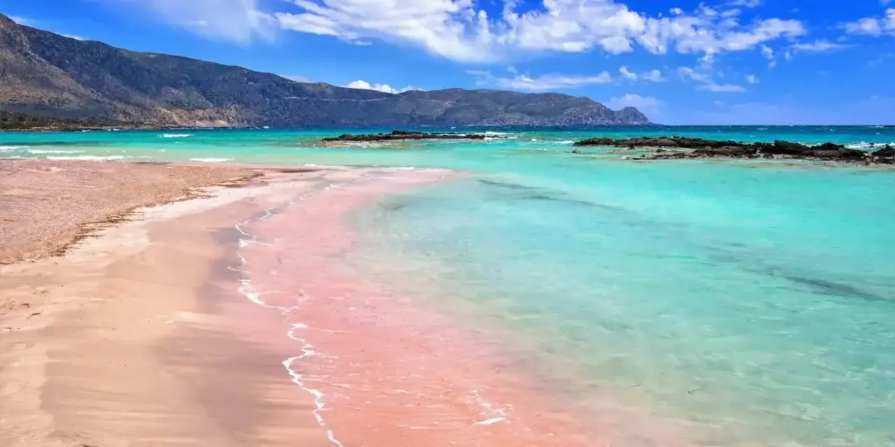 Różowa plaża Elafonisi z turkusową wodą i górami w tle. Idealne miejsce na relaks.
