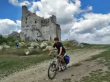 Młody rowerzysta przemierza malownicze **Jura Krakowsko-Częstochowska szlaki**, mijając ruiny zamku na tle błękitnego, chmurnego nieba.