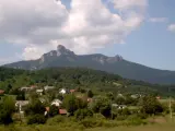 Widok na malowniczą wieś u podnóża góry Klek. Domy z czerwonymi dachami wtulone w zieleń, a nad nimi majestatyczny, skalisty szczyt.