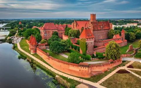 Malbork, największy zamek w Polsce, majestatycznie wznosi się nad rzeką Nogat. Czerwona cegła i strzeliste wieże tworzą imponujący widok.