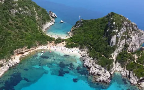 Malownicze **Korfu plaże** w zatoce, z turkusową wodą, zielonymi wzgórzami i tłumem plażowiczów.