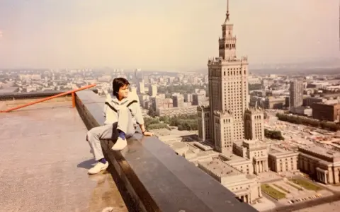 Młody mężczyzna siedzi na dachu, patrząc na panoramę Warszawy. W tle Pałac Kultury i Nauki, który wtedy był najwyższym budynkiem, zanim powstał Marriott.
