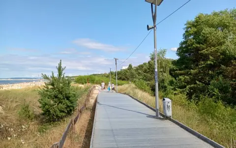 Spacer po promenadzie w Świnoujściu. Widok na plażę, morze i zielone drzewa. Atrakcje dla spacerowiczów.