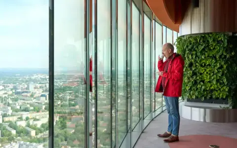 Mężczyzna pije kawę, podziwiając panoramę Wrocławia z tarasu widokowego. Sprawdź Sky Tower Wrocław cennik, by poznać ceny biletów.