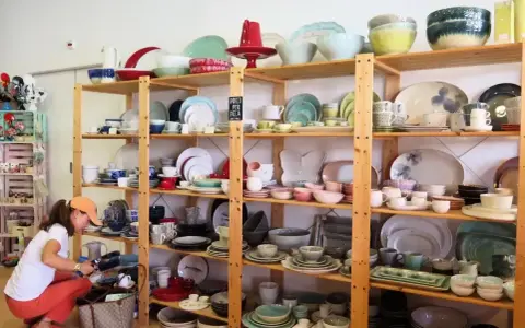 Kobieta wybiera ceramiczne naczynia, idealne pamiątki, które warto co przywieźć z Portugalii. Kolorowe talerze, miski i filiżanki na drewnianych półkach.