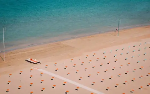 Pusta plaża w Rimini z rzędami pomarańczowych parasoli i łodzią ratowniczą.