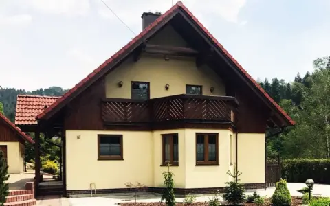 Jasny dom z drewnianymi elementami i balkonem, otoczony zielenią. Może to być dom Adama Małysza w Wiśle.