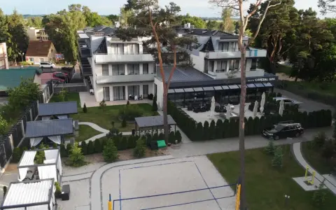 Nowoczesny hotel Cristal Spa z basenem i kortem do siatkówki plażowej, otoczony zielenią.