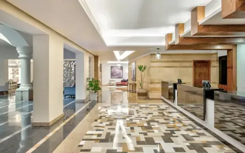 Eleganckie lobby hotelu Radisson z recepcją, ozdobnymi kolumnami i mozaikową podłogą. Radisson individuals witają tu gości.
