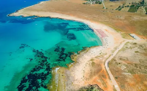 Widok z lotu ptaka na turkusowe morze i piaszczyste bari plaże z rzędami parasoli.
