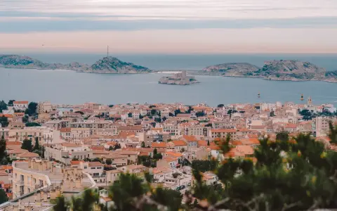 Widok na miasto z dachami i morzem w tle, z widocznym zamkiem na wyspie. To piękne **Marseille**.