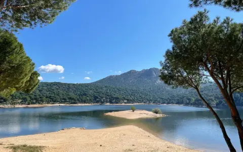 Piękna, piaszczysta plaża nad jeziorem w pobliżu Madrytu, otoczona sosnowym lasem i górami.