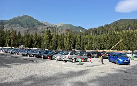 Parking przy wejściu na Morskie Oko. Rząd samochodów pod górskimi szczytami i gęstym lasem.
