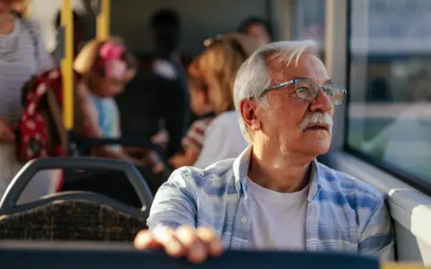 Starszy pan w okularach, podróżujący autobusem w Szczecinie, zastanawia się, czy 70 latek płaci za komunikację miejską.