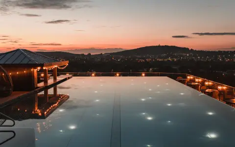Zachód słońca nad miastem, basen na dachu hotelu w Polsce, oświetlony girlandami i lampkami.
