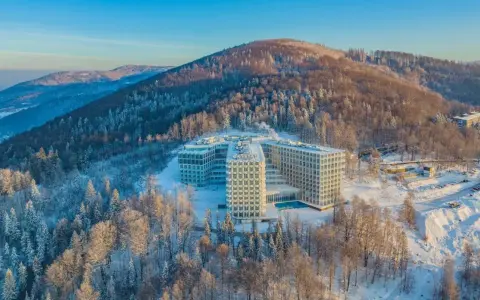 Nowoczesny hotel Crystal w zimowej scenerii, otoczony ośnieżonym lasem. To idealne miejsce na wypoczynek w Wiśle, górskim kurorcie.