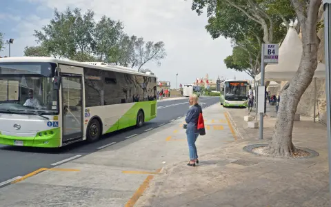 Kobieta czeka na autobus na Malcie. W tle widać autobusy, w tym jeden jadący w kierunku lotniska.