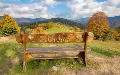 Drewniana ławka z napisem "Ciechocinek" na tle jesiennych gór i zielonych wzgórz. Widok na Beskid Sądecki.