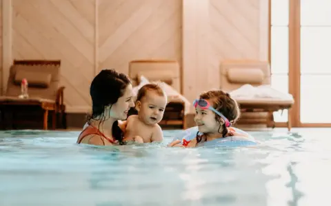 Rodzina cieszy się basenem w hotelu dla dzieci w Wiśle. Mama z dwójką dzieci pluska się w wodzie, tworząc radosne wspomnienia.