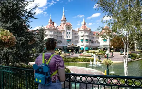 Dziewczyna z plecakiem w kształcie Myszki Miki podziwia zamek w Disneyland Paris. Bilety do parku już kupione, czas na przygodę!
