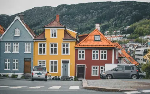 Kolorowe domy w Norwegii, jak te niebieski, żółty i czerwony, to jedna z wielu ciekawostek o Norwegii. W tle widać wzgórza i zabudowania.
