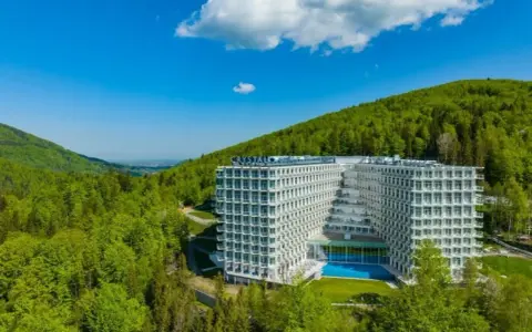 Nowoczesny Crystal Mountain Hotel Wisła otoczony zielonymi wzgórzami, z basenem i tarasami.