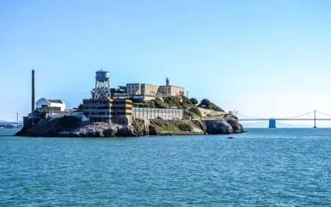 Słynne więzienie Alcatraz na skalistej wyspie, z charakterystyczną wieżą ciśnień i mostem w tle.