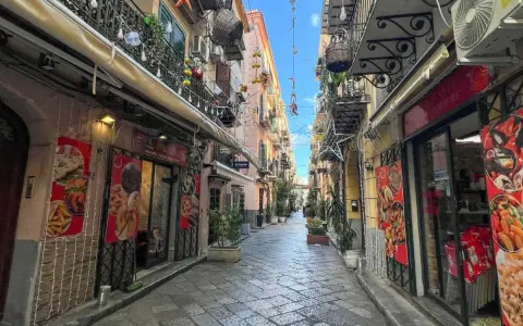 Wąska uliczka w Palermo, stolicy Sycylii, z restauracjami i balkonami ozdobionymi lampkami.