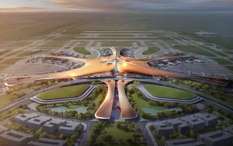 Futurystyczny terminal lotniska, przypominający rozgwiazdę, z samolotami na płycie. To największe lotnisko na świecie, z nowoczesną architekturą i otaczającą zielenią.