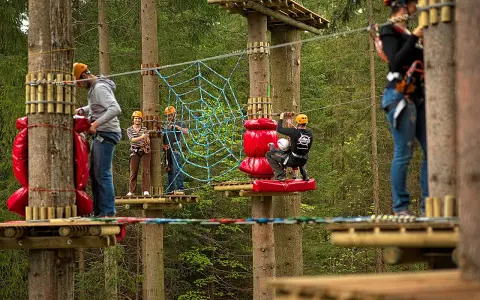 Park linowy Base Camp Istebna: ludzie na platformach wśród drzew, pokonują przeszkody, w tym pajęczynę.