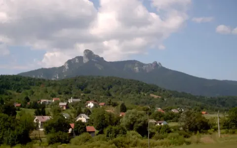 Widok na malowniczą wieś u podnóża góry Klek. Domy z czerwonymi dachami wtulone w zieleń, a nad nimi majestatyczny, skalisty szczyt.