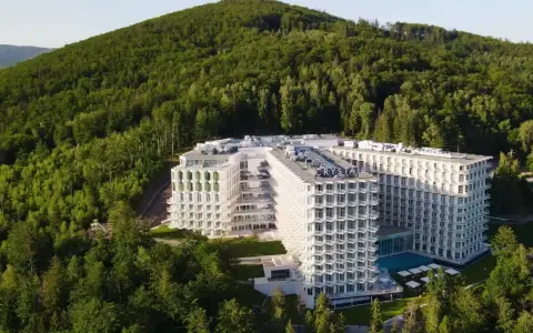 Nowy hotel w Wiśle, Crystal Mountain, wtopiony w zielone zbocze góry. Nowoczesna architektura z licznymi balkonami i basenem.