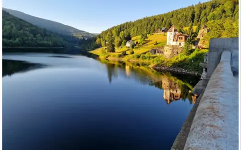 Spokojna tafla jeziora odbija zamek i zalesione wzgórza czeskich Karkonoszy.