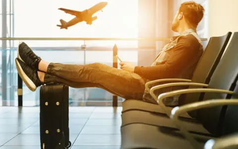 Mężczyzna z nogami na walizce czeka na lotnisku. Samolot startuje. Czyżby czekał na niego, czy to tylko efekt **overbooking**?