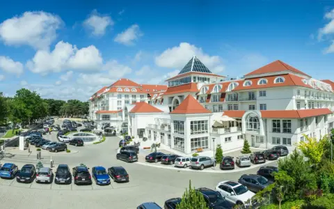 Elegancki hotel 5 gwiazdkowy nad morzem z przestronnym parkingiem pełnym samochodów.