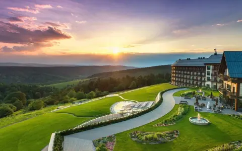 Hotel Arłamów z basenem i tarasem, otoczony zielonymi wzgórzami o zachodzie słońca. Ile pokoi ma hotel Arłamów? Tego nie widać, ale jest ich wiele!