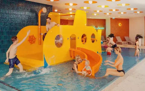 Rodzina bawi się w hotelu z aquaparkiem dla dzieci w górach. Żółta łódź podwodna ze zjeżdżalnią to centrum wodnych atrakcji.