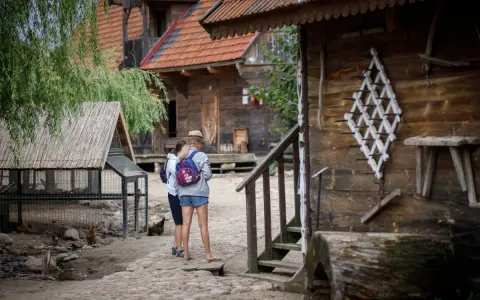 Dwie dziewczyny zwiedzają skansen, który może być częścią oferty hotelu bon turystyczny. W tle drewniane chaty i kurnik.