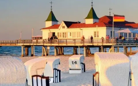 Plaża z koszami i molo, gdzie widać budynek restauracji i niemiecką flagę. Atrakcje po niemieckiej stronie Świnoujścia zachęcają do spacerów.