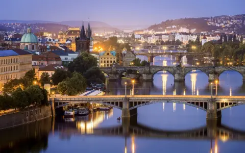 Praga nocą, z wieloma mostami na Wełtawie i oświetlonymi budynkami. Ciekawe ciekawostki o Czechach czekają na odkrycie w tym magicznym mieście.