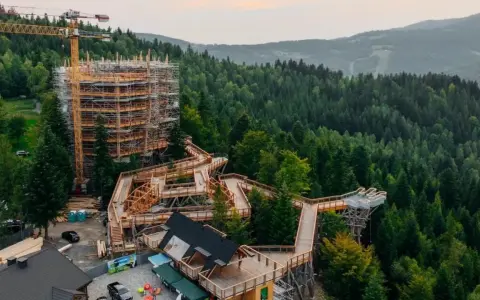Drewniany taras widokowy w Wiśle wznosi się nad lasem, oferując wspaniałe widoki. W tle widać las i góry.