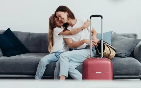 Mama i córka przytulają się na kanapie, obok walizka. Wszyscy, którzy chcą zameldować się w hotelu, mogą tu poczuć się jak w domu.